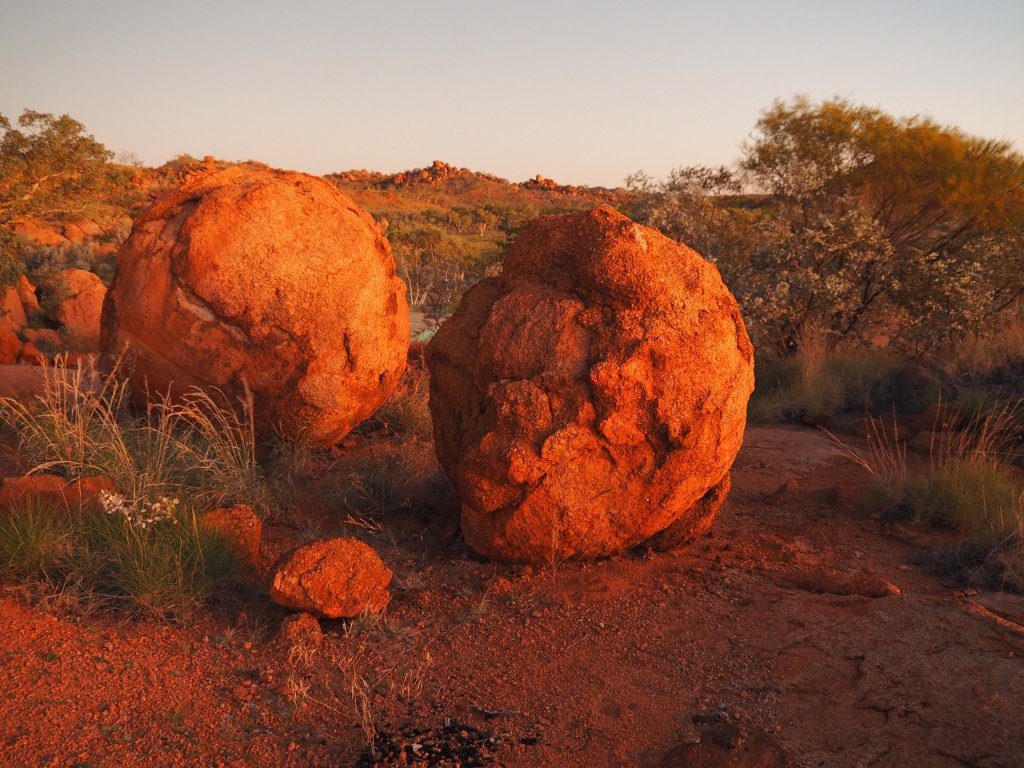 two large rust-coloured spherical rocks in an outback landscape